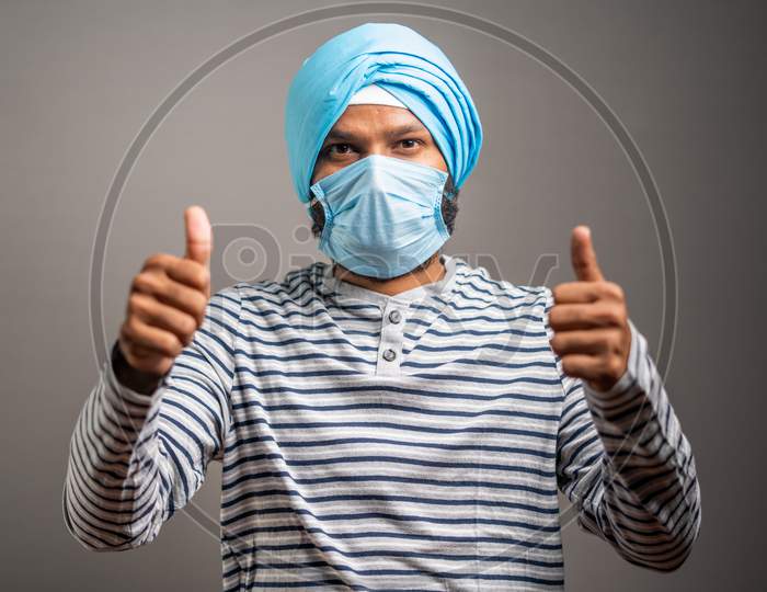 Young Sikh Man With Medical Face Mask Recommending To Wear Face Mask By Showing Thumbs Up Gesture During Coronavirus Covid-19 Pandemic.