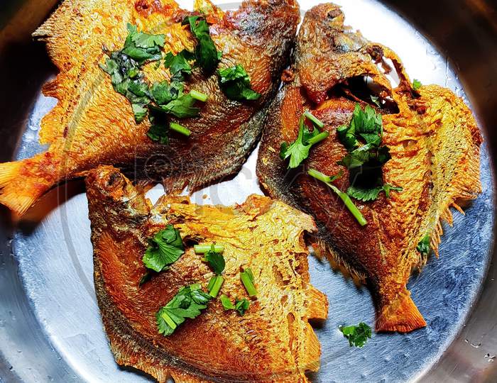 Three fried pomfret fish on the dish in a restaurant at Kolkata, India. Focus on subject.