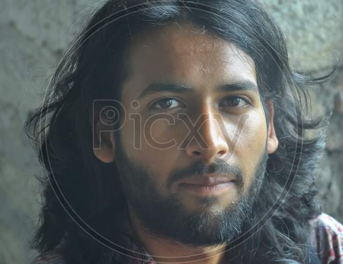 Close up shot of a attractive Indian young man face with beard and long hair. A guy looking at camera