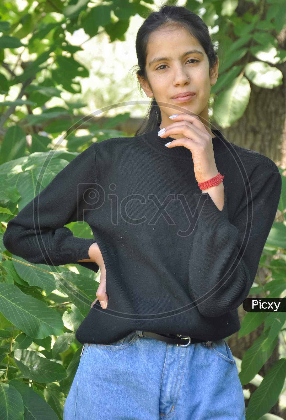 Close-up portrait of a pretty north Indian young girl standing in nature posing with one hand on chin and the other one on hips with looking at camera