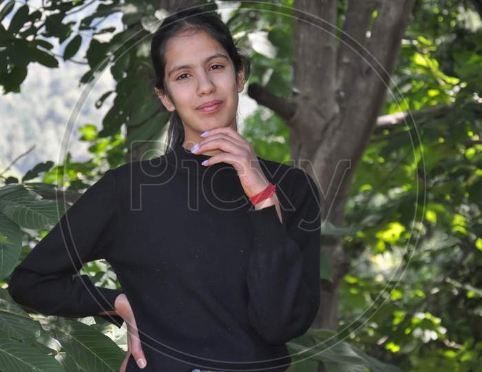 Close-up portrait of a pretty north Indian young girl standing in nature posing with one hand on chin and the other one on hips with looking at camera