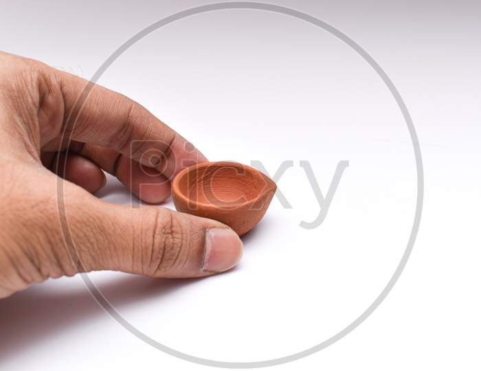 Placing Diya Or Clay Oil Lamp With Fingers For Diwali Festival Of Lights With White Background
