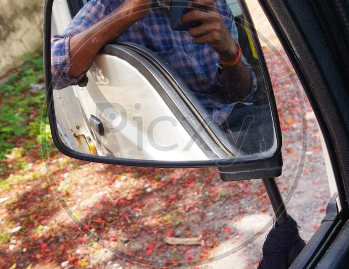 A guy taking pictures from inside the car by the use of side mirror