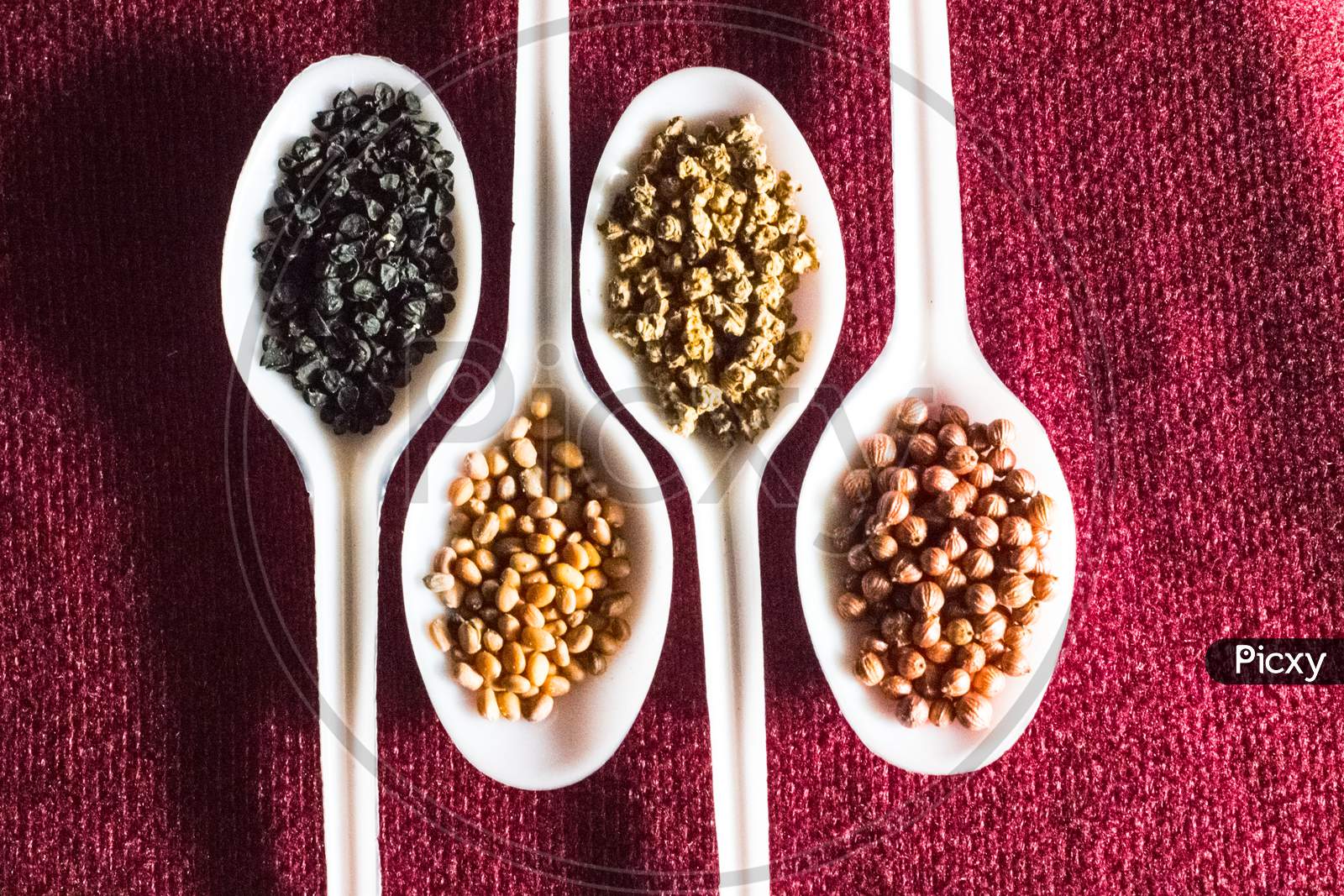 Seeds Of Onion, Unknown, Ladies Finger (Bhindi), Dhania(Coriander) In White Plastic Spoon.