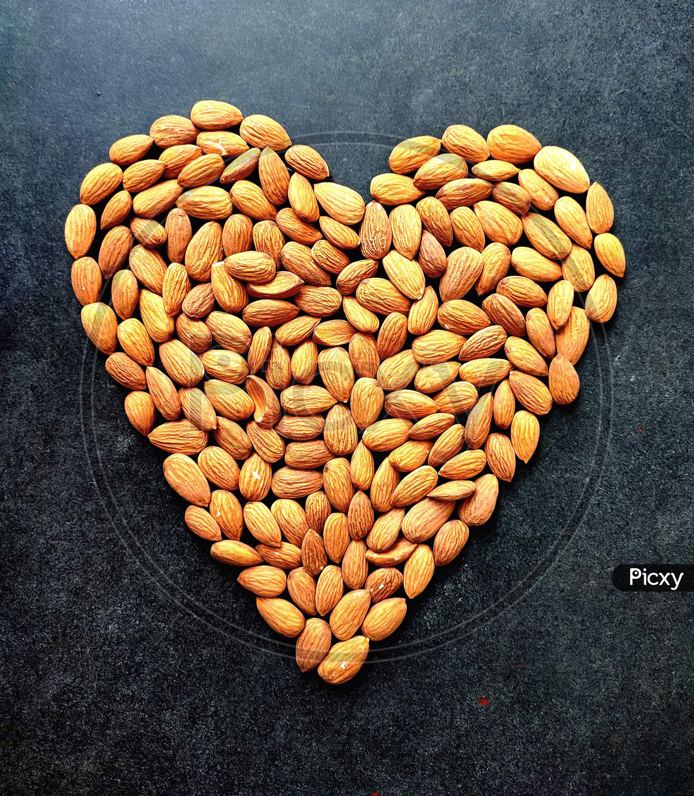 Almond Nuts Forming A Heart-Shape Isolated On Black Texture Wooden Background, Valentine Day Love Formed Heart.