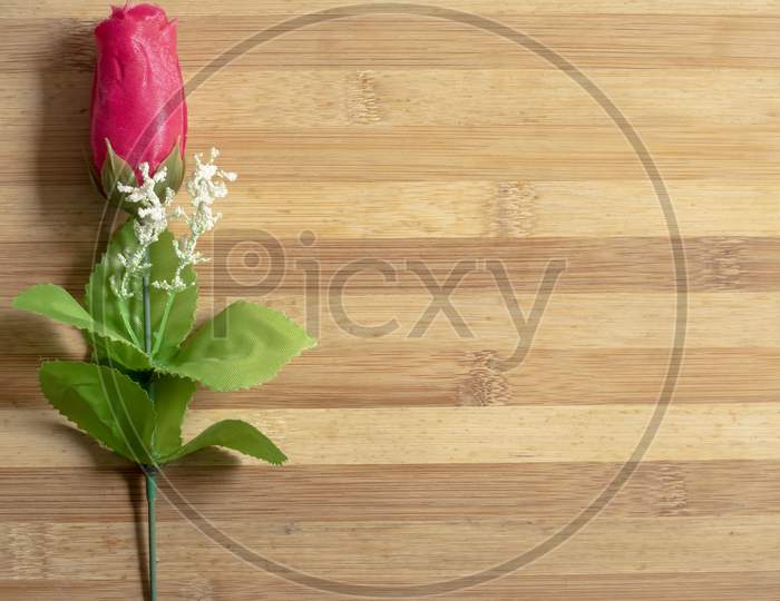 Red Plastic Roses On A Wooden Table