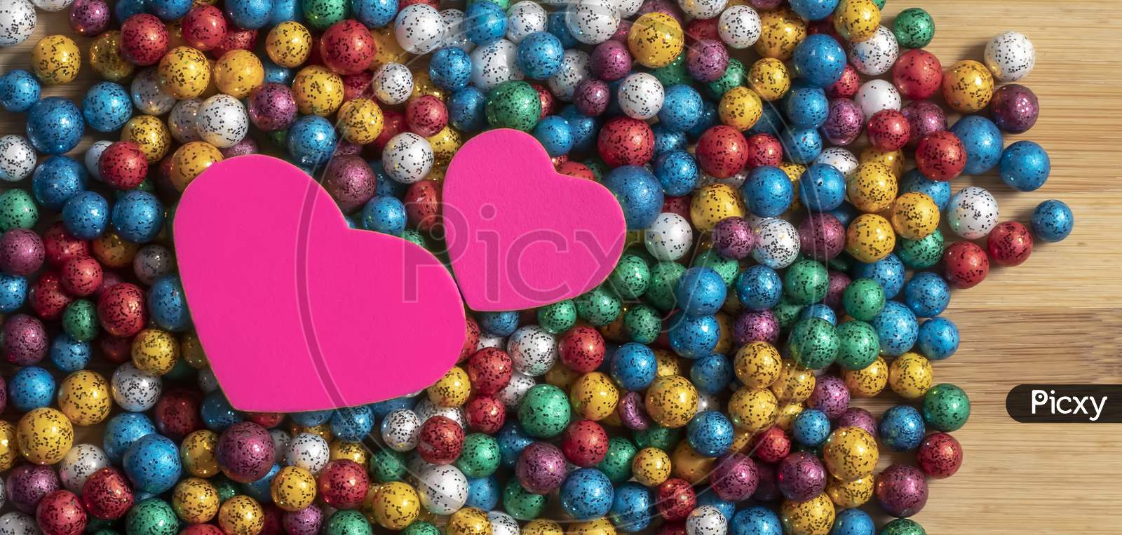 Valentine'S Day Background. Multicolor Small Size Thermocol Decorative Balls With Two Pink Hearts On Top Of A Wooden Table