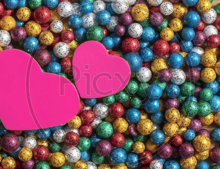 Valentine'S Day Background. Multicolor Small Size Thermocol Decorative Balls With Two Pink Hearts On Top Of A Wooden Table