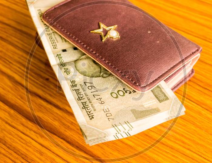 Indian Five Hundred (500) Rupee Cash Note In Brown Color Wallet Leather Purse On A Wooden Table. Business Finance Economy Concept. Side Angel View With Copy Space Room For Text On Left Side Of Image.