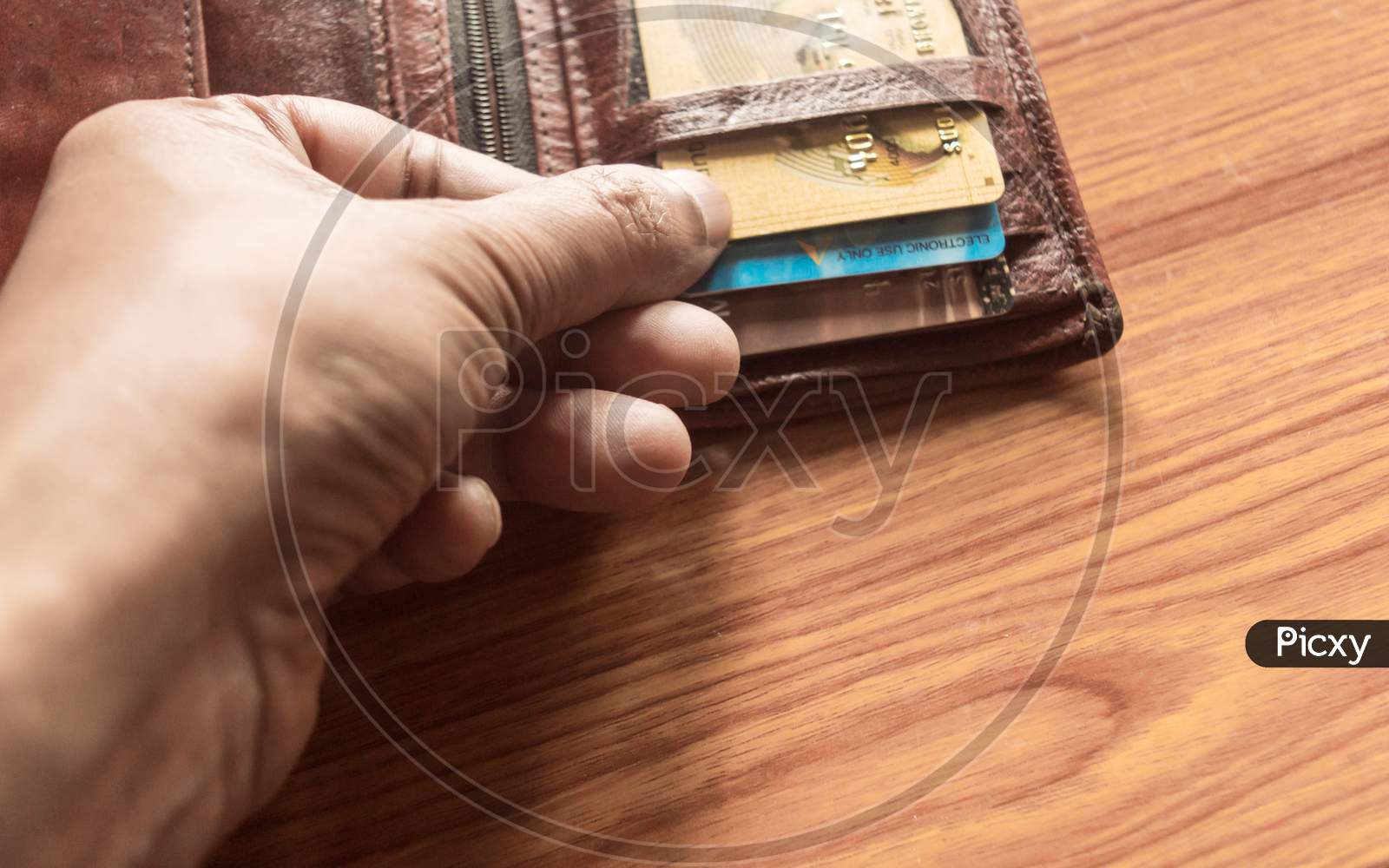 Man'S Hand Pulls Out A Credit Card Out Of A Money Purse. Cropped Close-Up Image. Wood Table Background.