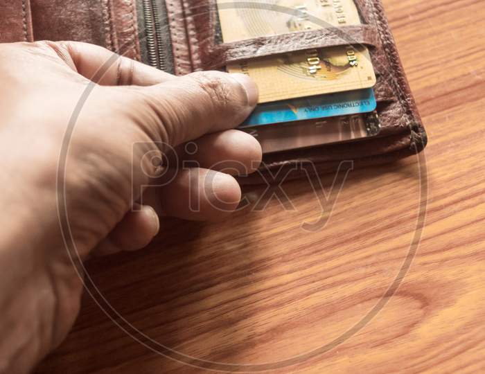Man'S Hand Pulls Out A Credit Card Out Of A Money Purse. Cropped Close-Up Image. Wood Table Background.