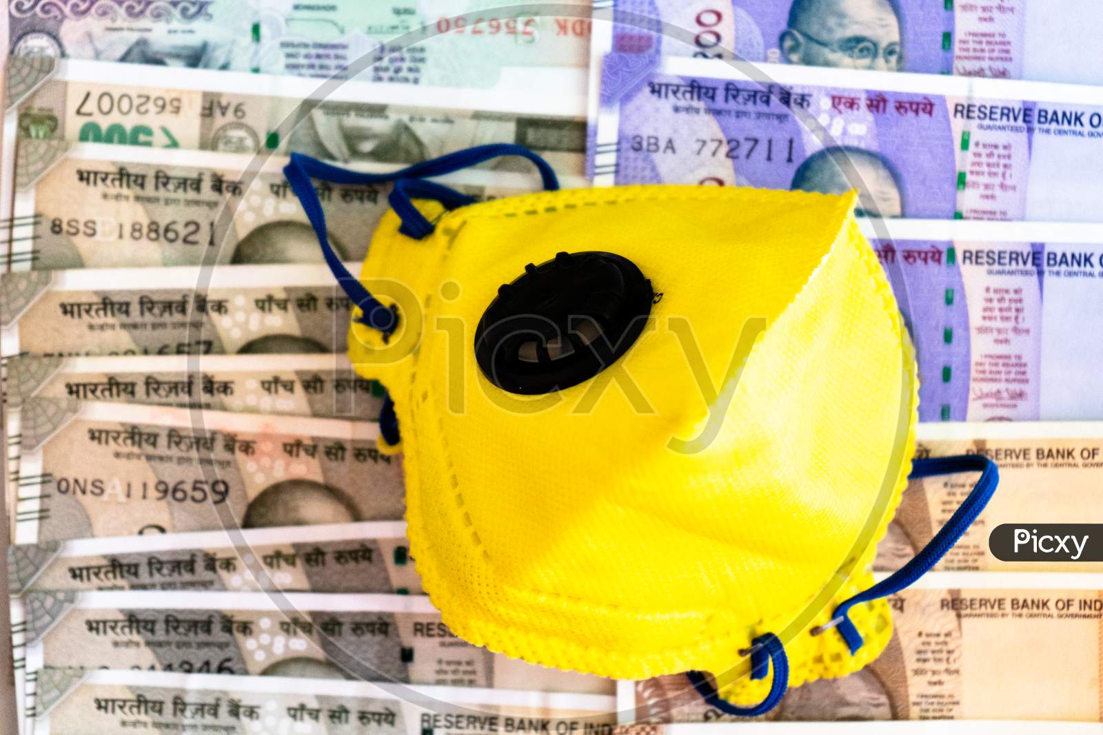 Safety And Business Essentials Yellow Mask And Sanitizer Placed On Bed Of Indian Currency