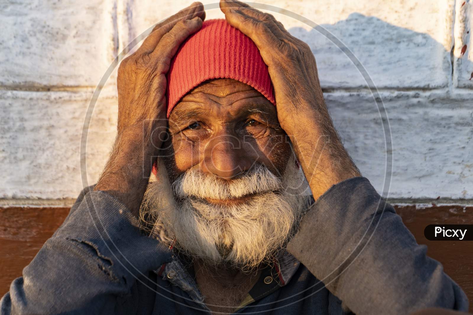 Portrait Of An Old Indian Man, Old Aged Man With Wrinkles On His Face Holding His Face With His Hands And Sitting In The Sunlight.