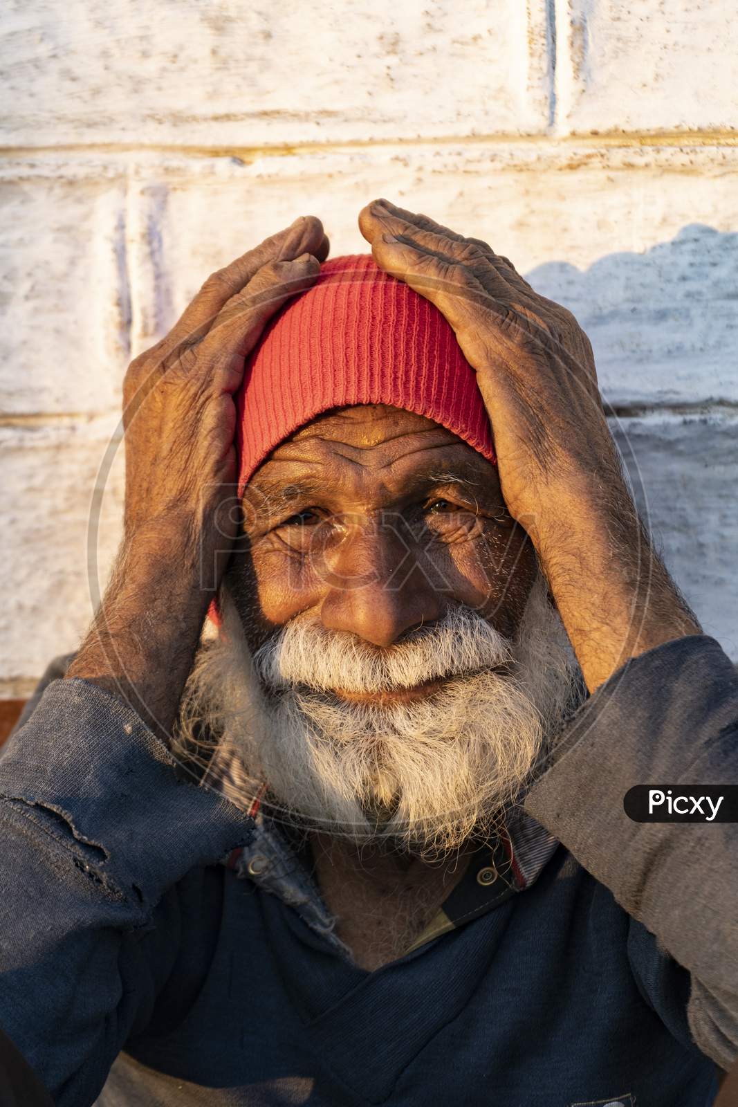 Portrait Of An Old Indian Man, Old Aged Man With Wrinkles On His Face Holding His Face With His Hands And Sitting In The Sunlight.