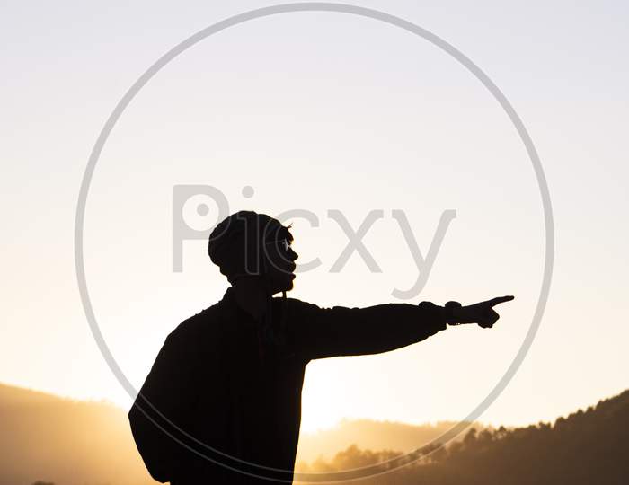 Silhouette Of A Young Boy Standing In The Fields And The Beautiful Mountains In The Background Captured During Sunset.