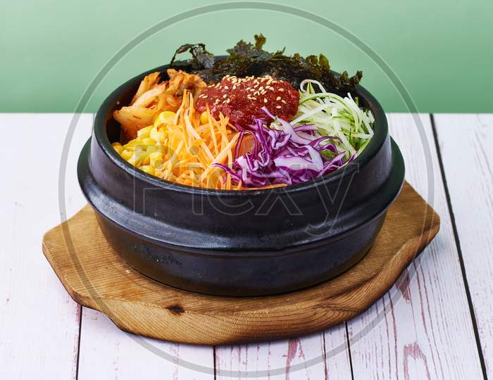 Korean Food Rice Bibimbap With Vegetables, Beef And Teriyaki In A Black Bowl On Wood Tbale Background